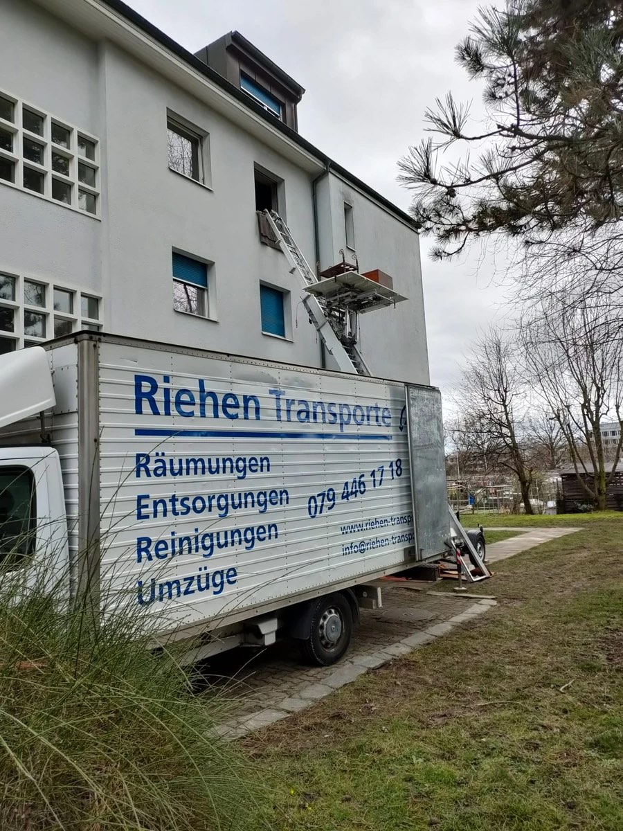 Beschriftetes Fahrzeug der Riehen Transporte GmbH mit ausgefahrenem Möbellift bis in den oberen Stock bei einer Räumung